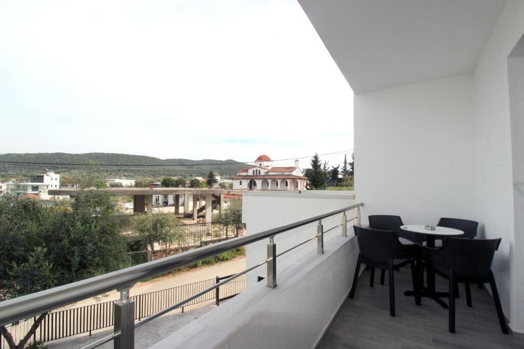 Un balcon avec une table et des chaises, donnant sur un bâtiment surmonté d’un dôme et offrant une vue sur des collines.