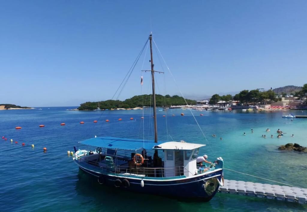 A boat docked at a harbor with clear blue water, a small cabin, and a few people on the shore.