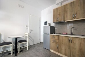 Cocina compacta con armarios de madera, un refrigerador, un microondas, un lavamanos y una pequeña mesa redonda con dos sillas.