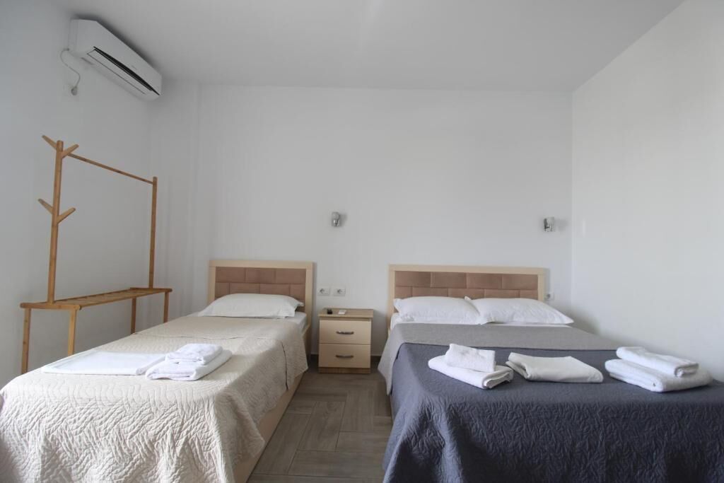 A hotel room with two beds, a wooden sideboard, a small bedside table, and an air conditioning unit.