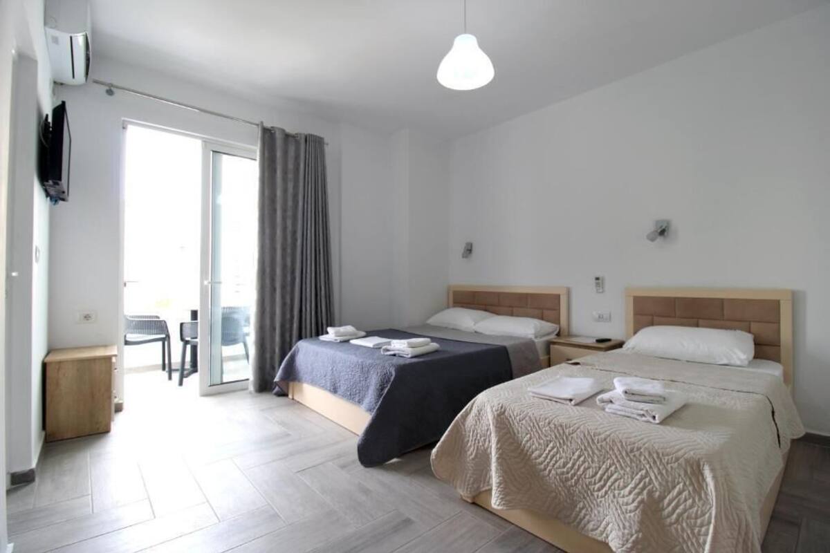 A hotel room with two beds, a TV, a ceiling light, and a sliding glass door leading to an outdoor area.