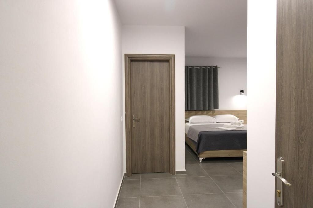 Corredor estreito que dá para um quarto com cama, porta de madeira e cortina.