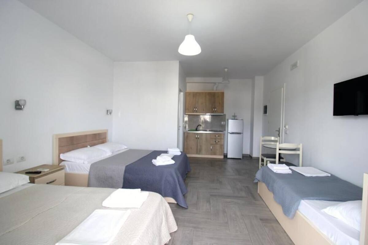 A hotel room with two beds, a kitchenette, a TV, and a wooden floor.