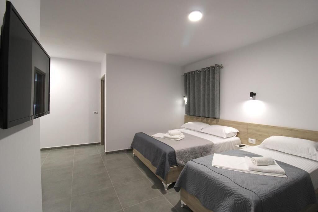 A hotel room with two beds, a flat-screen TV, a wall-mounted light, and a curtain.