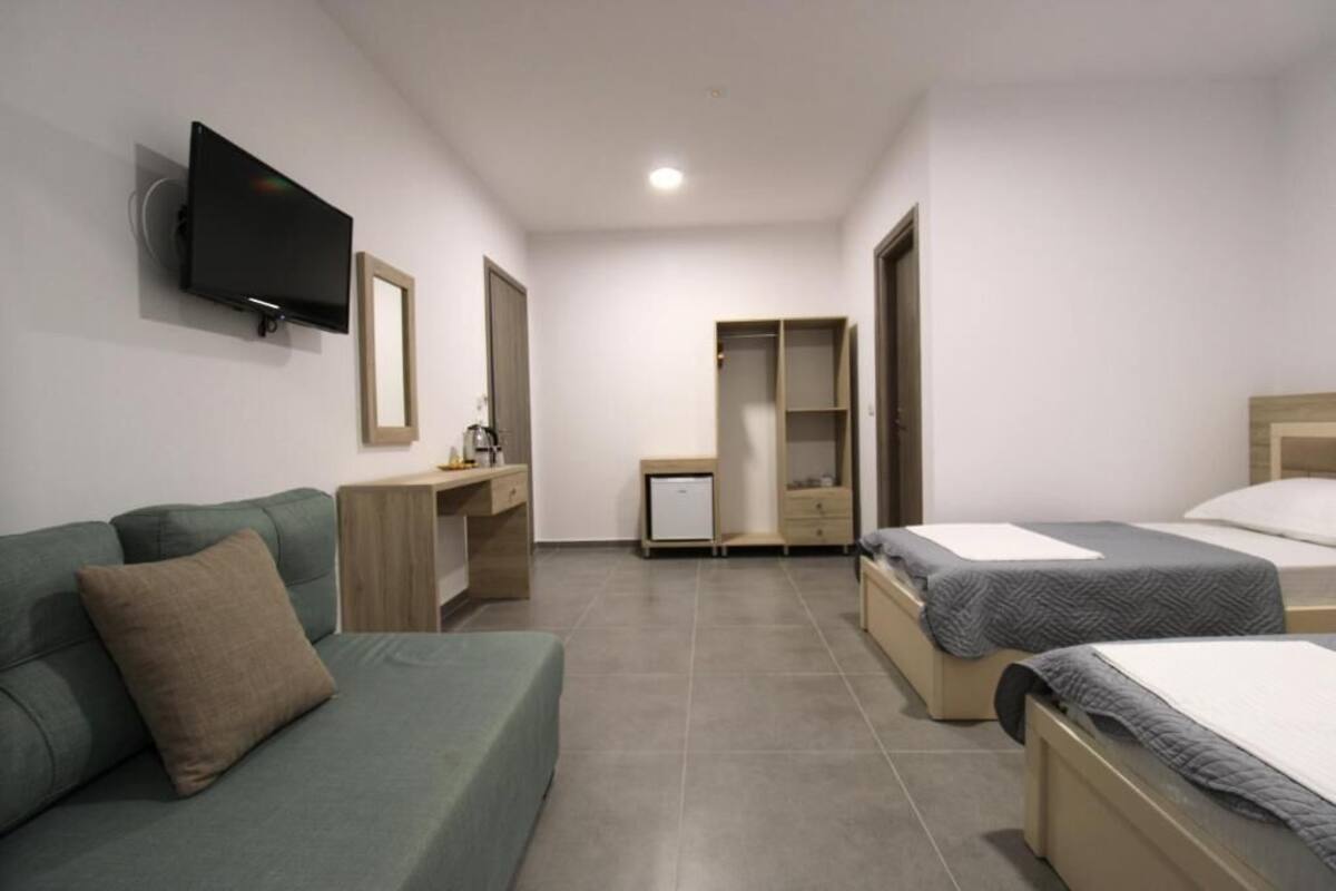 A hotel room with a green sofa, a bed, a desk with a chair, a television mounted on the wall, and a wardrobe.