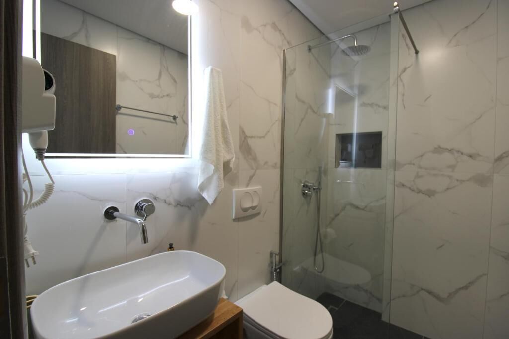 A bathroom with a white sink, a mirror, a shower, and a toilet.