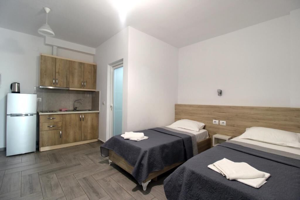 A compact hotel room with two beds, a kitchenette, and a bathroom.
