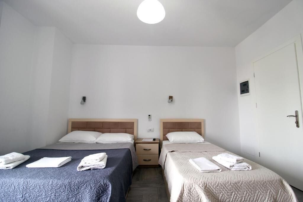 A room with two beds, each with a headboard, a nightstand, and a wall-mounted light fixture.