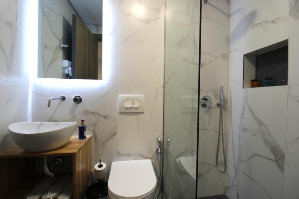 Un baño moderno con un lavamanos grande blanco, un inodoro y una zona de ducha con mampara de vidrio.