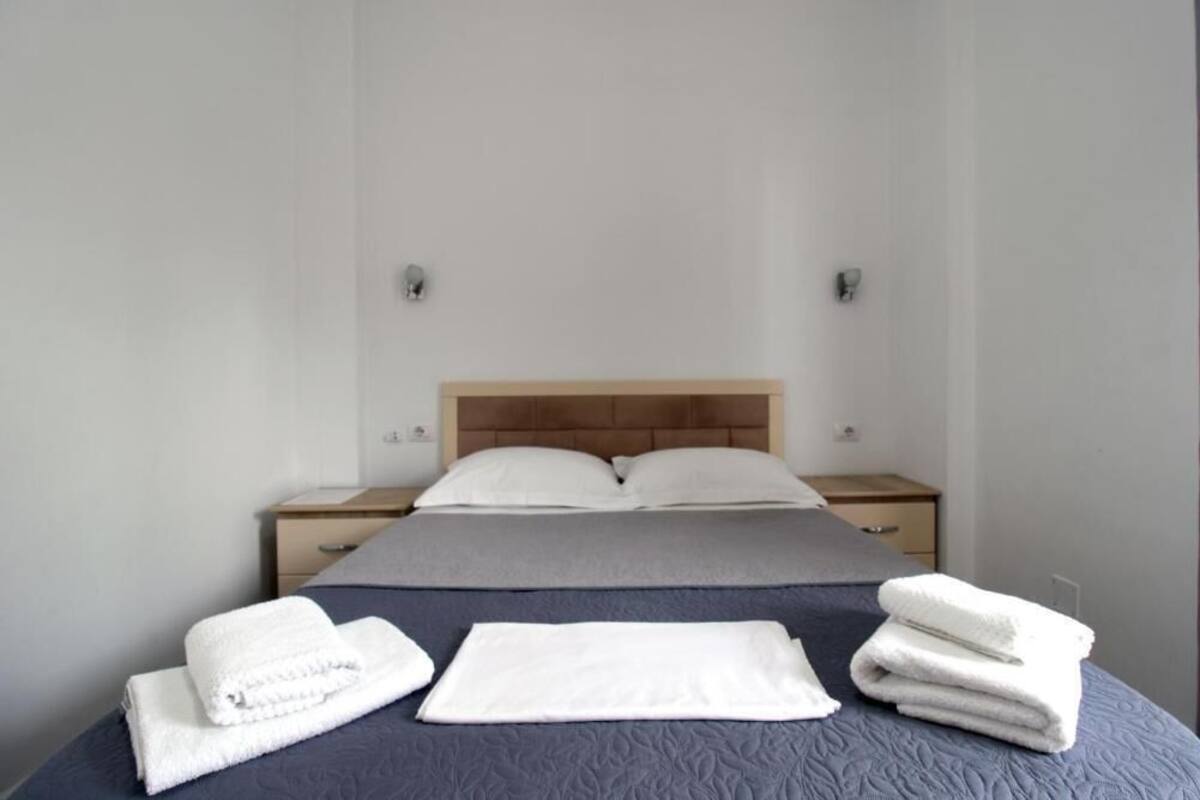 A neatly made bed with a headboard, two bedside tables, and a stack of folded towels.