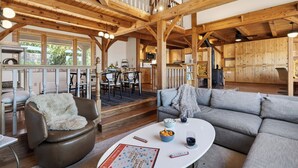 Ein großzügiger Wohnbereich mit hoher Holzdecke, einem Esstisch mit Stühlen, einer Couch und einem im Hintergrund sichtbaren Küchenbereich.