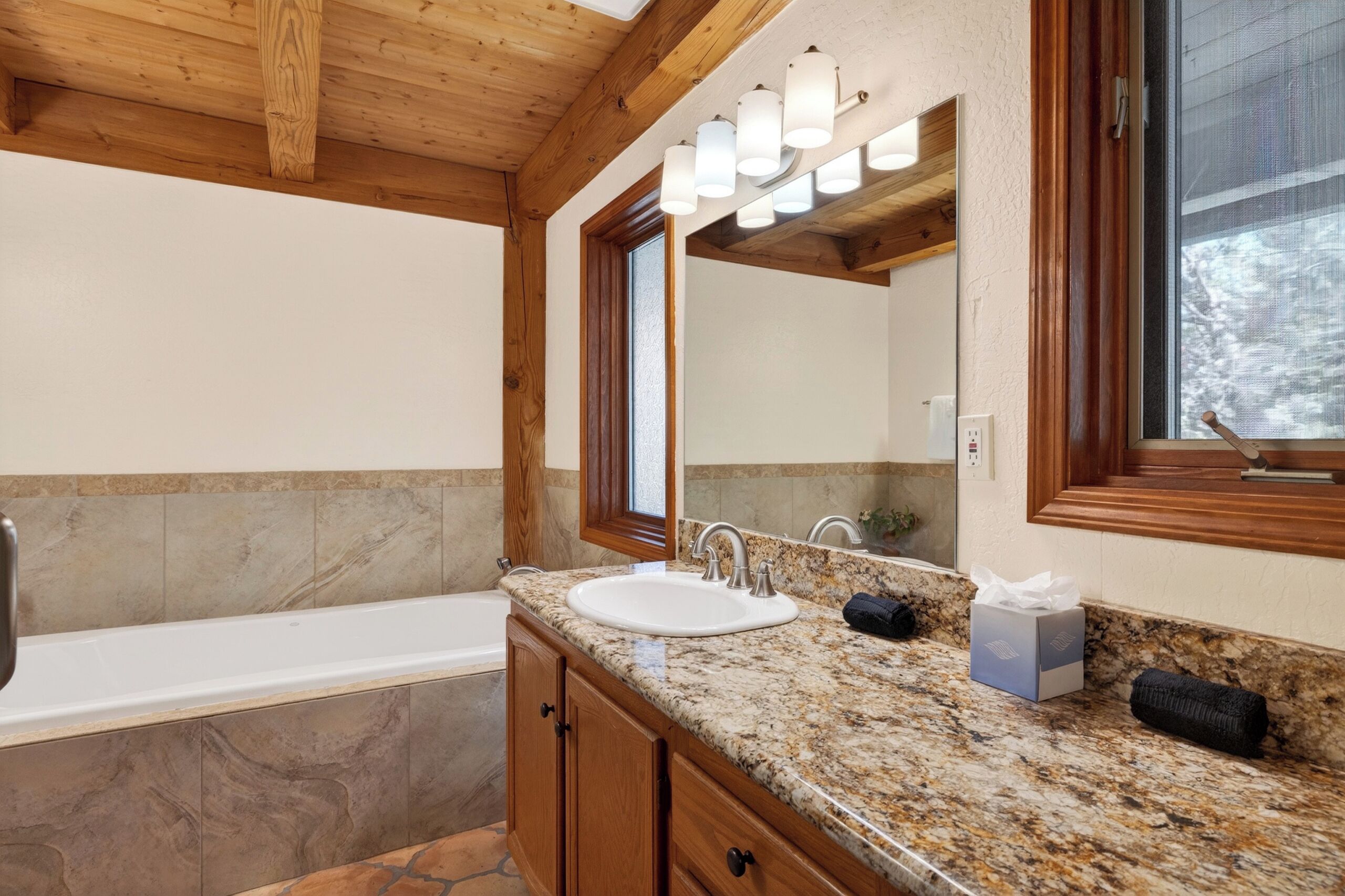 A bathroom with a granite countertop, two sinks, a mirror, and a window.