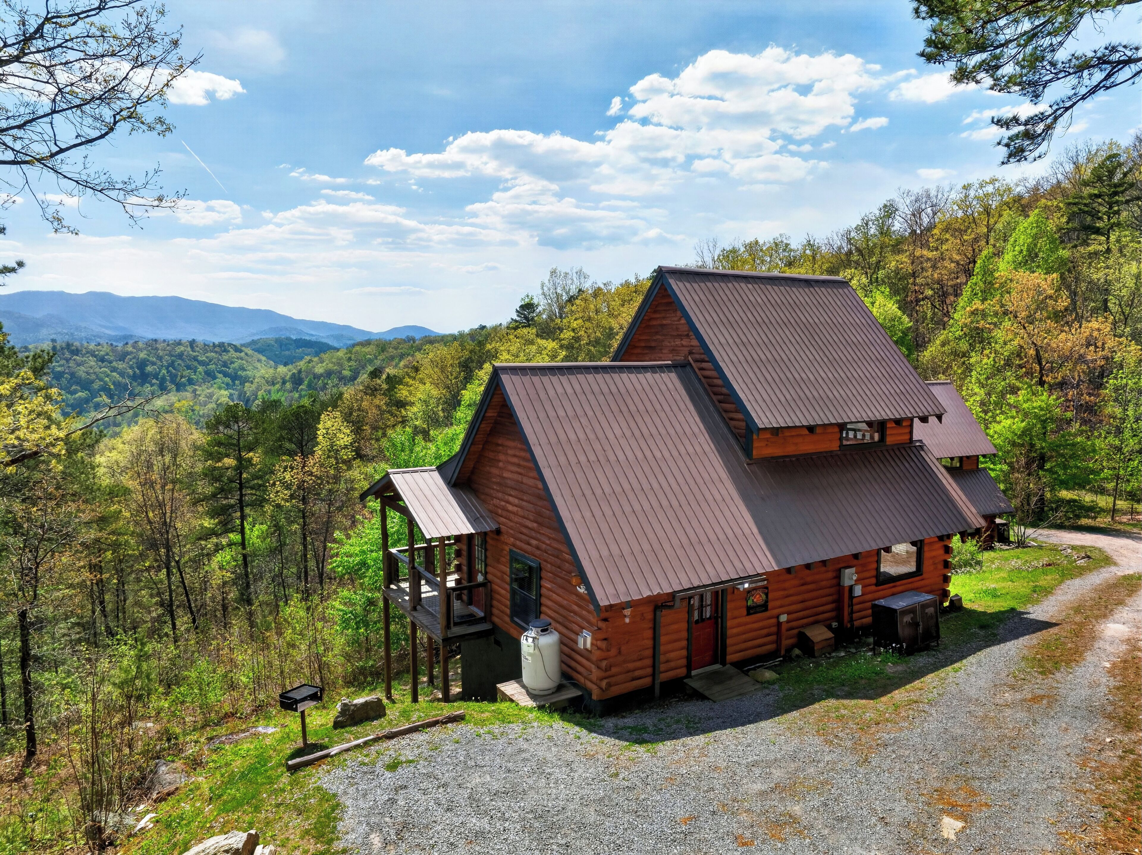 A cabin with a sloped roof, a porch, and a gravel driveway.