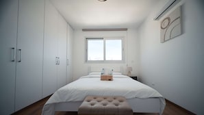 Una camera da letto con un letto, una panca, un comodino, una finestra e un condizionatore d'aria a muro.