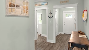 Un pasillo con piso de madera, decoración temática de playa y una puerta que da a otra habitación.