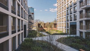 Ein moderner Gebäudekomplex mit mehreren Etagen, Balkonen und einem zentralen Innenhof mit Wegen und Grünflächen.