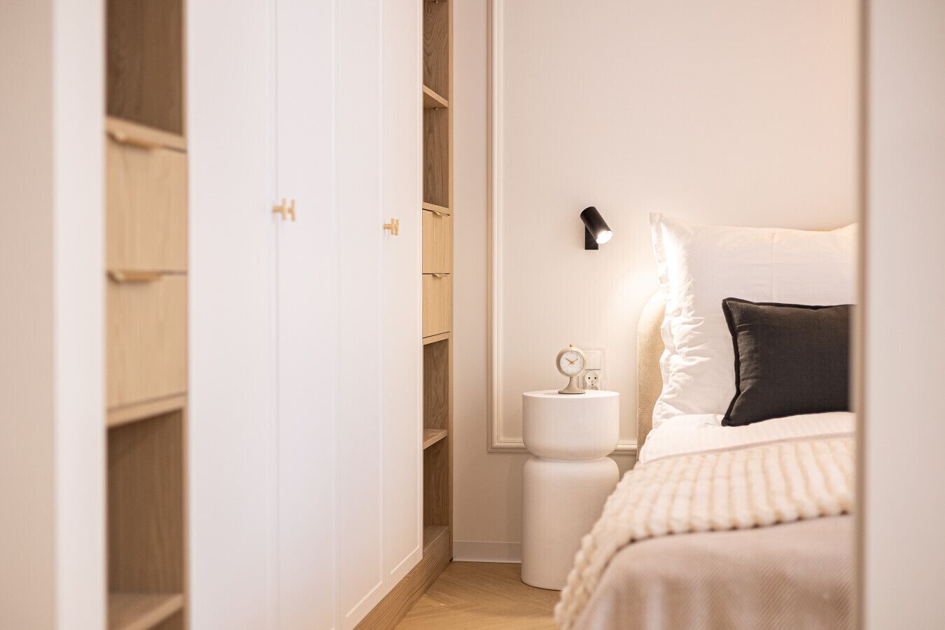 Un dormitorio con una cama, una mesita de noche con un reloj, una cómoda y un armario.