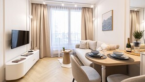 Ein modernes Wohnzimmer mit Fernseher, einer Couch, einem Esstisch mit Tellern und Gläsern sowie einem großen Fenster mit Vorhängen.