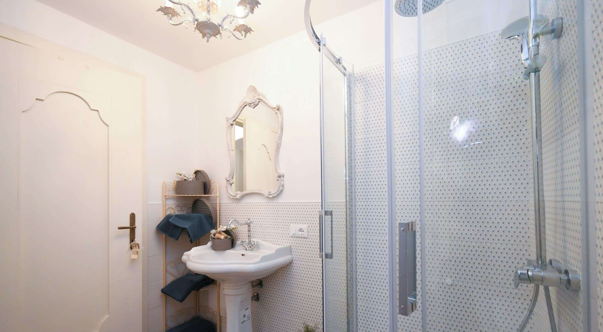 Une salle de bain dotée d’une douche à parois de verre, d’un lavabo sur colonne et d’un miroir encadré d’un cadre orné.