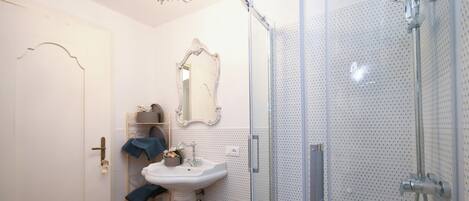 Une salle de bain dotée d’une douche à parois de verre, d’un lavabo sur colonne et d’un miroir encadré d’un cadre orné.