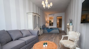 A living room with a sofa, a chair, a small table with plants, a cabinet, and a chandelier.