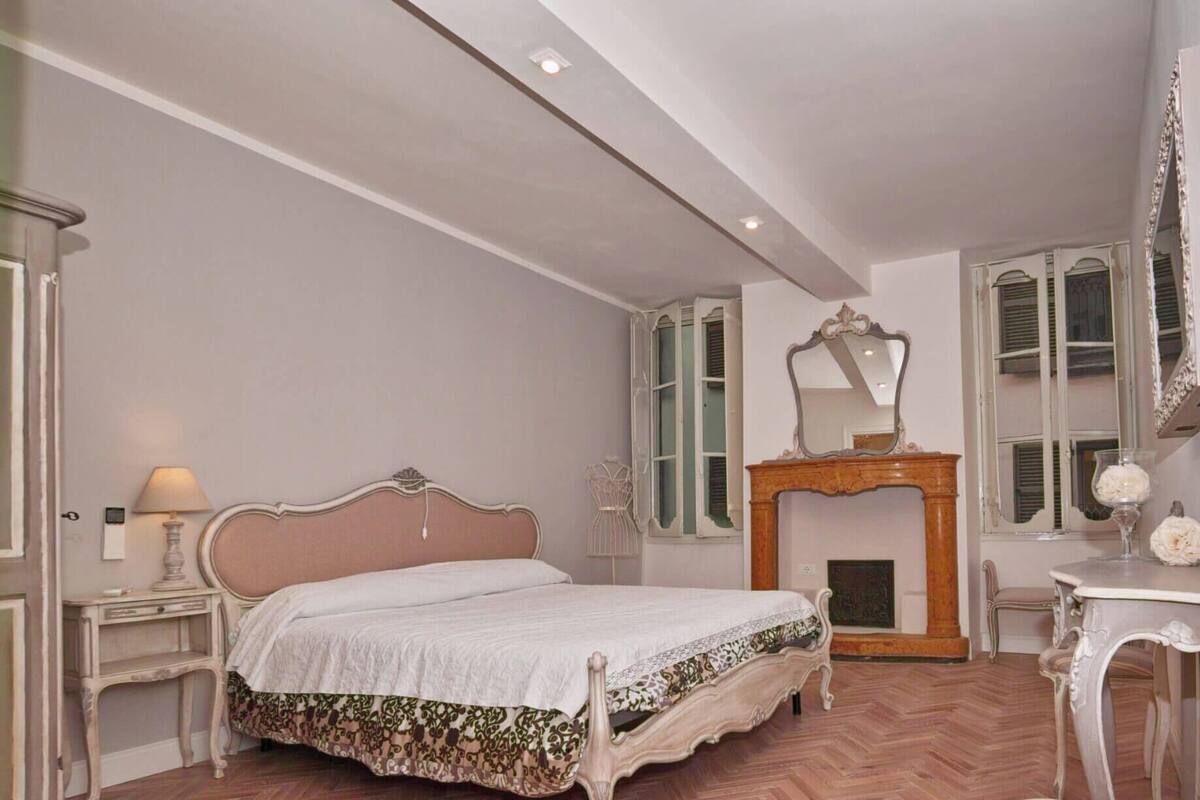A bedroom with a bed, a mirror, a fireplace, and a chair.