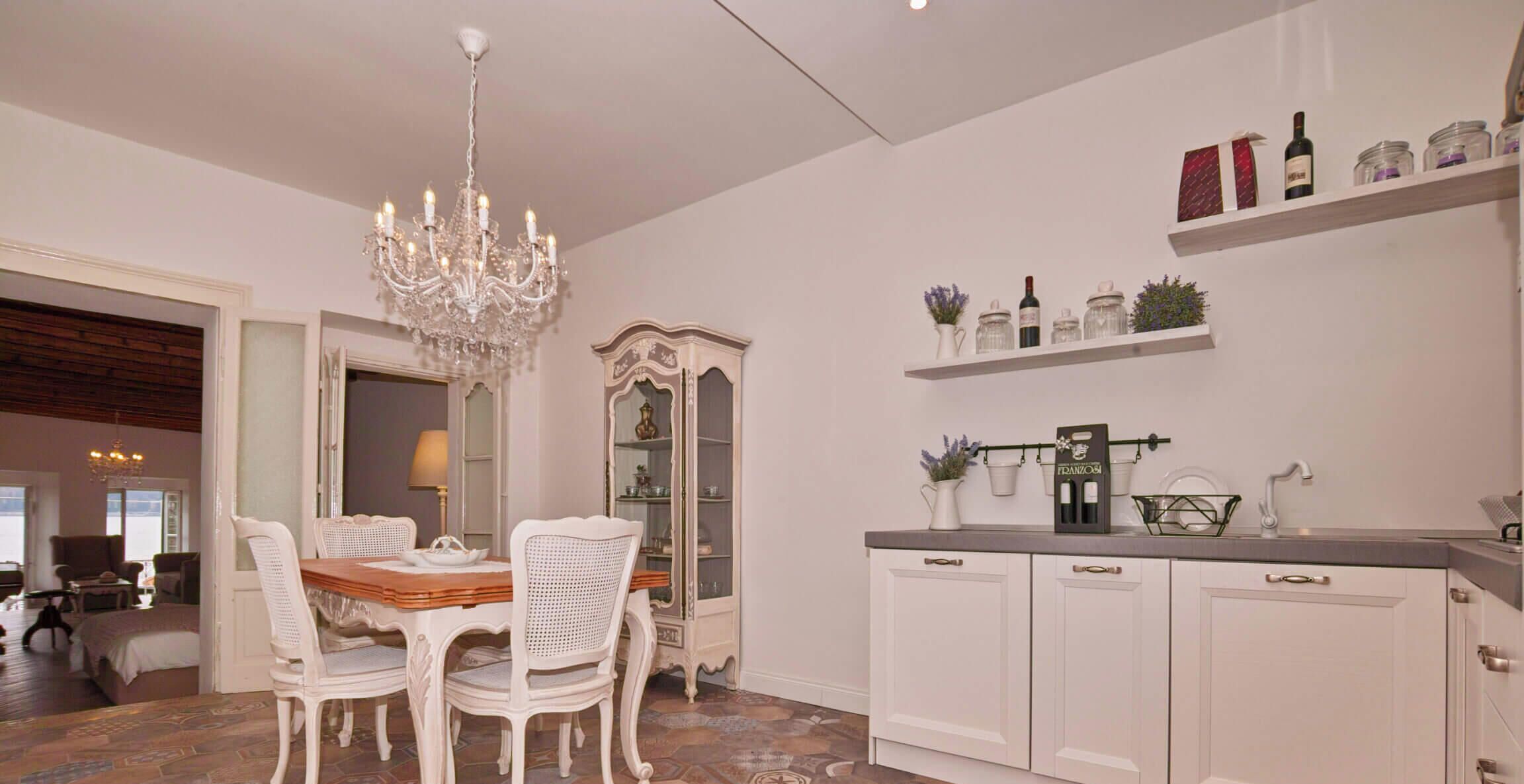 Un comedor con candelabro, sillas blancas, una mesa de madera y un aparador con estantes superiores.