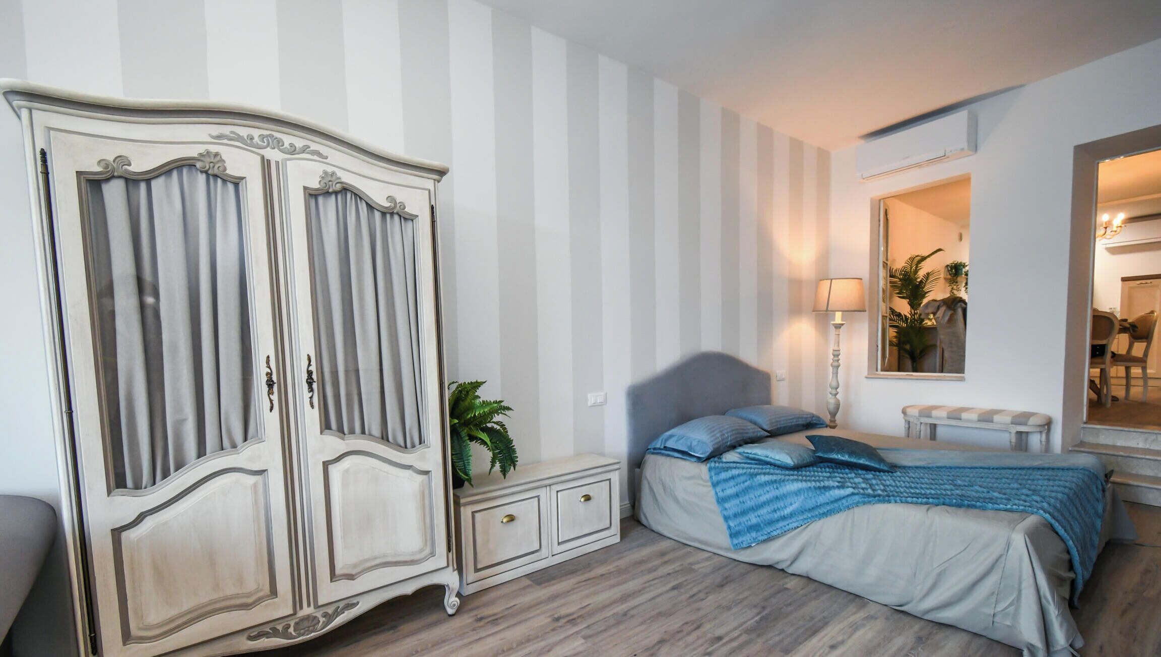 Ein Schlafzimmer mit Bett, Kleiderschrank, Nachttisch, Lampe und Spiegel.