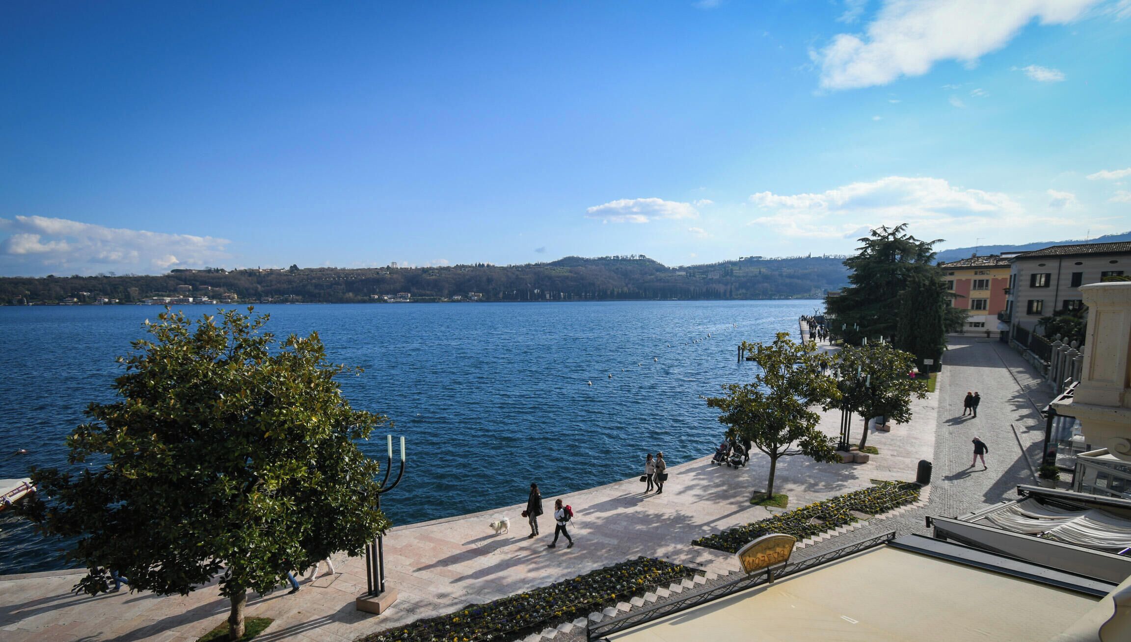 A waterfront promenade with a clear view of the lake, trees, and buildings in the background.