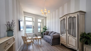 Una habitación con sofá, sillones, aparador, candelabro y vistas a una masa de agua a través de amplios ventanales.