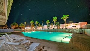 A swimming pool with lounge chairs and palm trees at night. - Walk to Beach + Boardwalk | Golf Cart Zone + Pool Access | Ocean View Efficiency (Port Aransas)