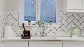 A kitchen with a herringbone tile backsplash, a window with a view, a sink, and a kettle on the counter.