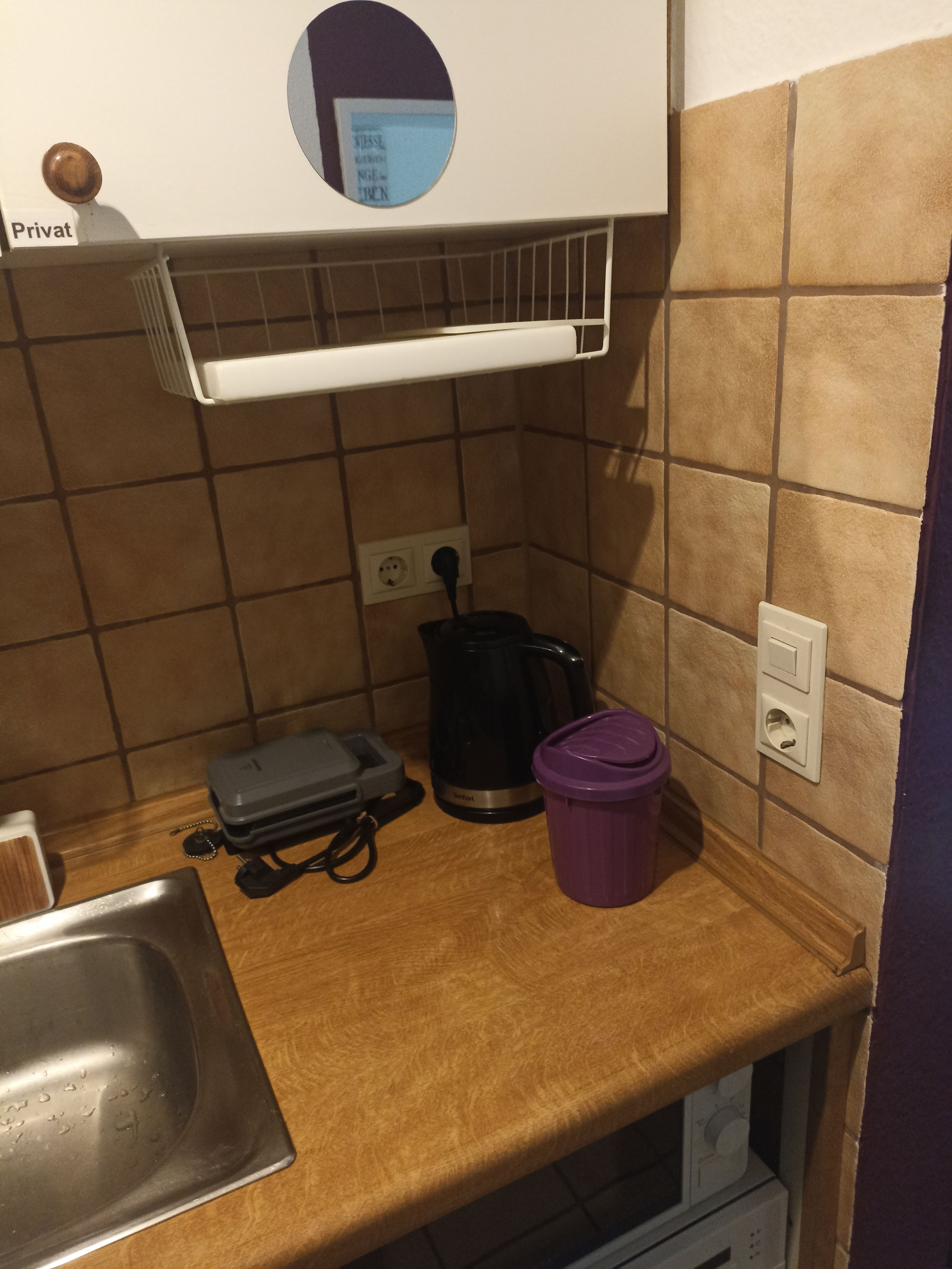 Pieni keittiönurkkaus, jossa on kahvinkeitin, vedenkeitin, roskakori ja pistorasiarakenne.
