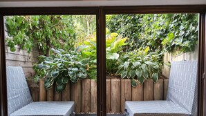 A patio with two patterned chairs, a wooden fence, and lush greenery. - Phil's Cozy Apartment: Self-Check-In Near the Airport, Free Parking, Airport Bus Stop (Leinfelden-Echterdingen)