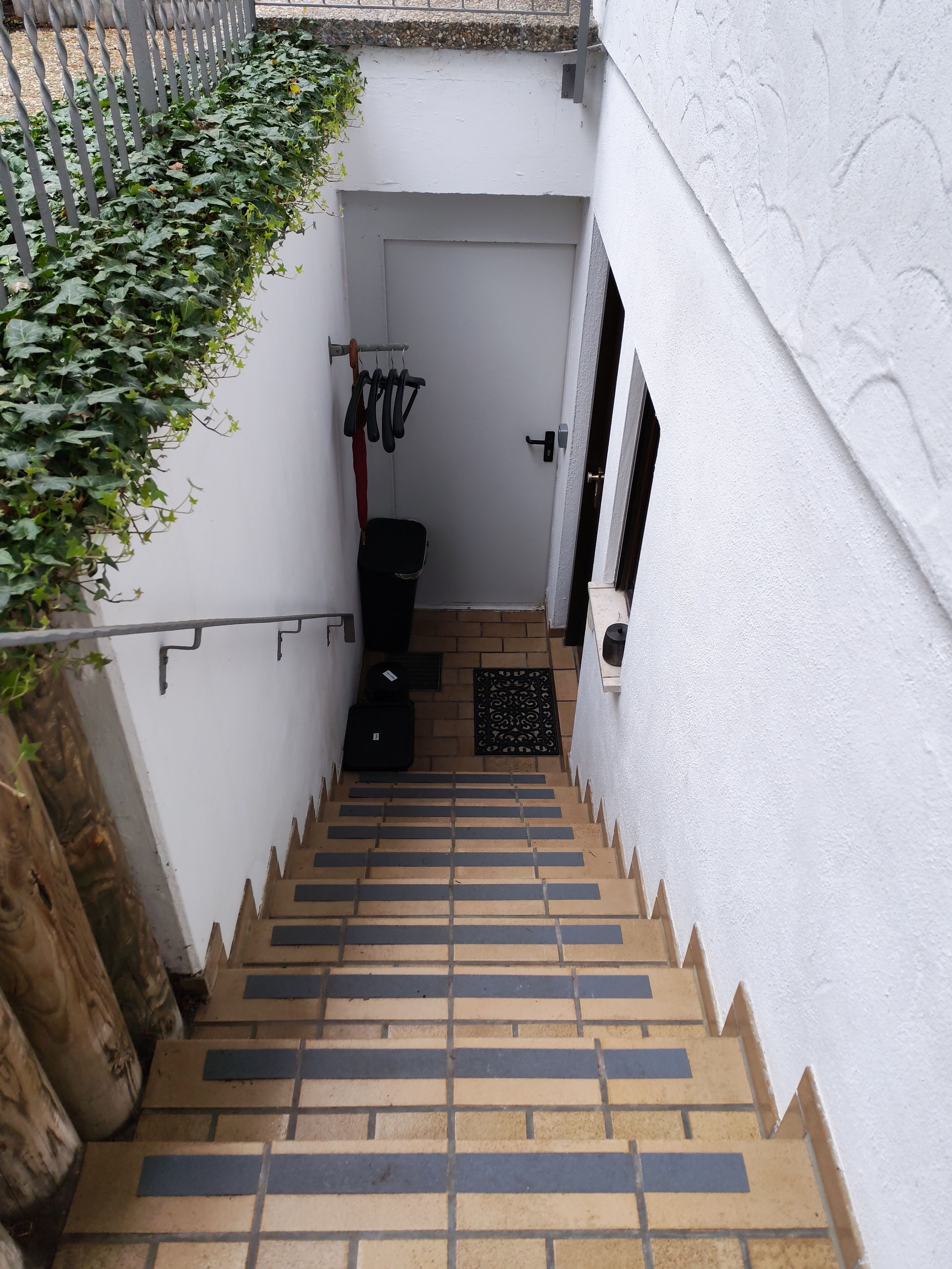Eine schmale Treppe mit Metallgeländer, einem schwarzen Mülleimer und einer Tür am oberen Ende.