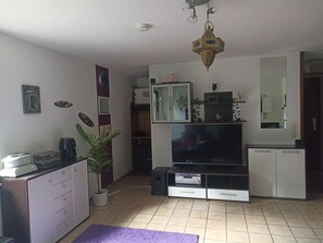 Una sala de estar con televisor de pantalla plana, armarios, cafetera y una planta en maceta.