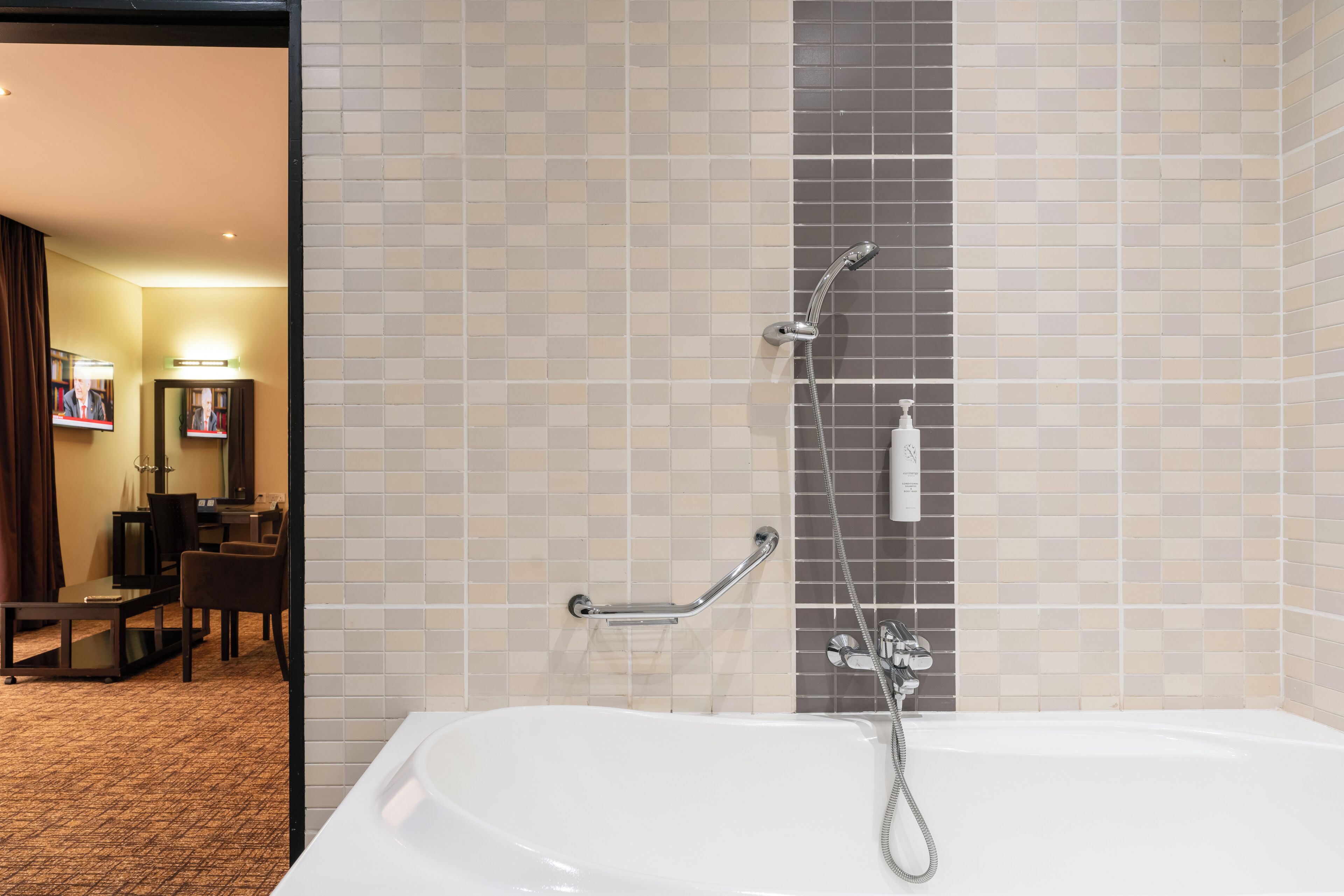 A hotel bathroom with a bathtub, a shower, and a handrail.