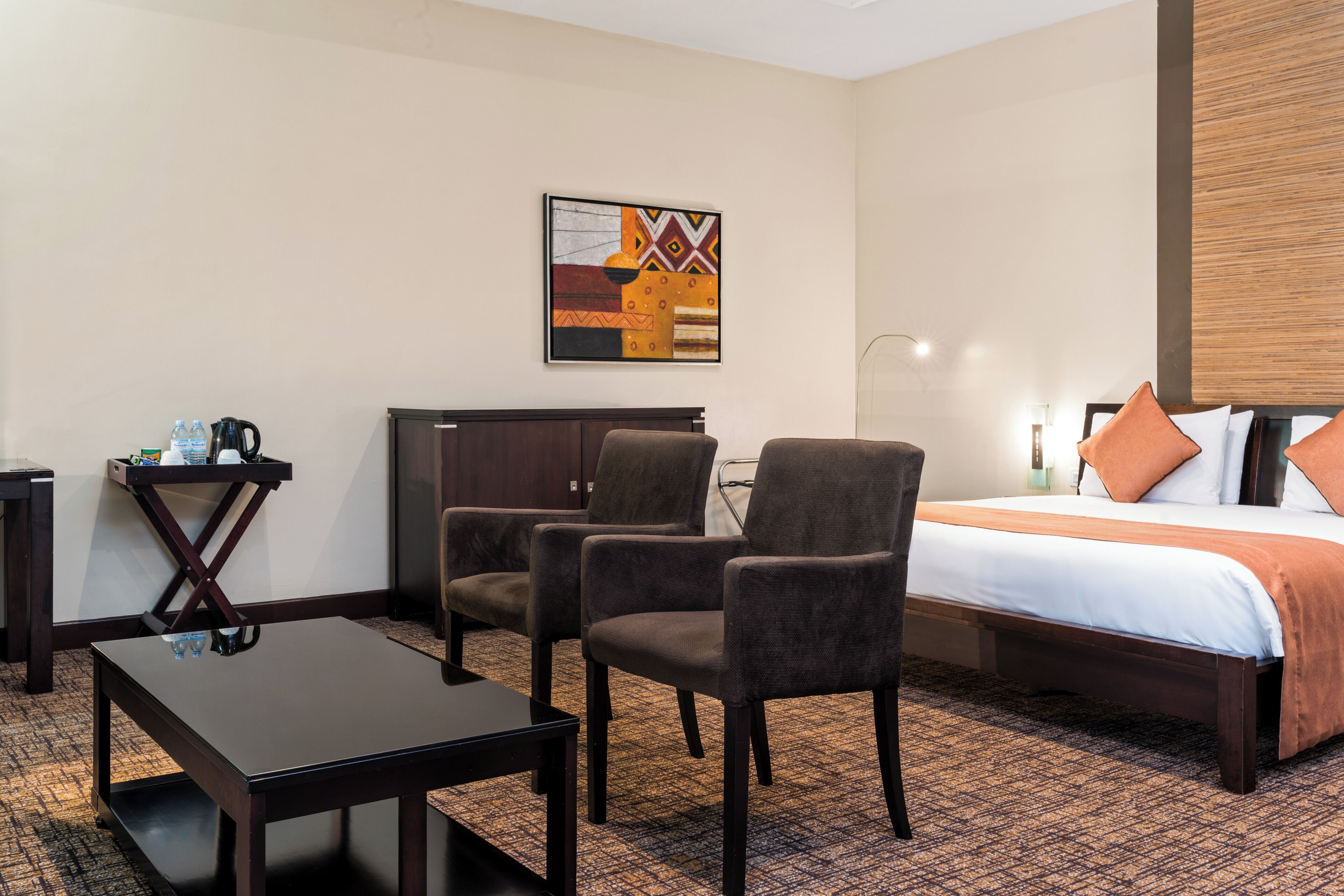 A hotel room with a bed, two armchairs, a small table, a coffee maker, and a painting on the wall.