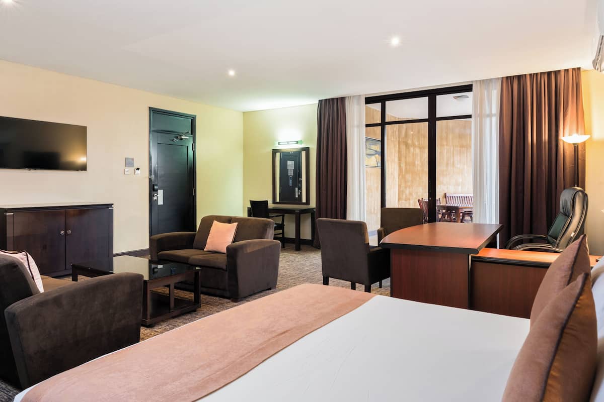 Habitación de hotel con cama, dos sillones, escritorio, televisor de pantalla plana, armario y ventana grande con cortinas.