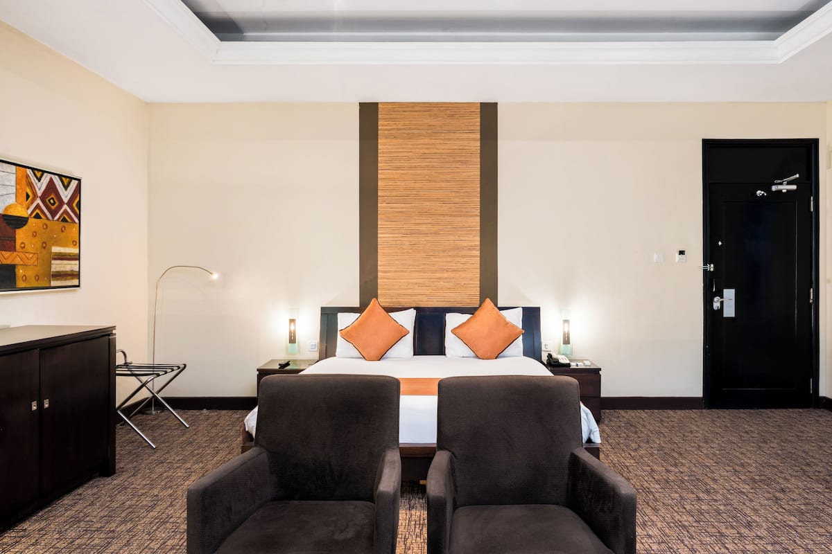 Una habitación de hotel con una cama, dos sillones, un escritorio, una lámpara y una puerta.
