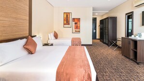 A hotel room with two beds, a desk, a wardrobe, and artwork on the wall. - Hotel 33 Kampala (Kampala)