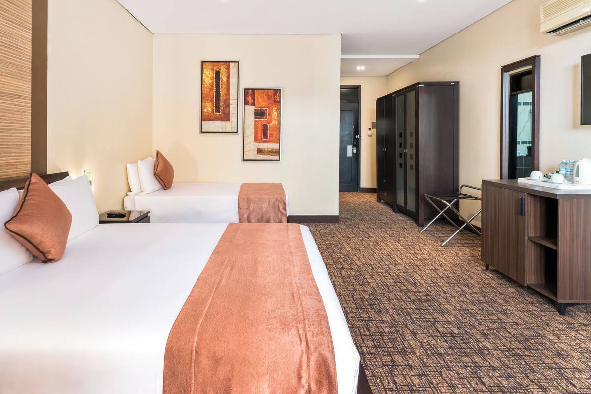 Habitación de hotel con dos camas, un escritorio, un armario y obras de arte en la pared.