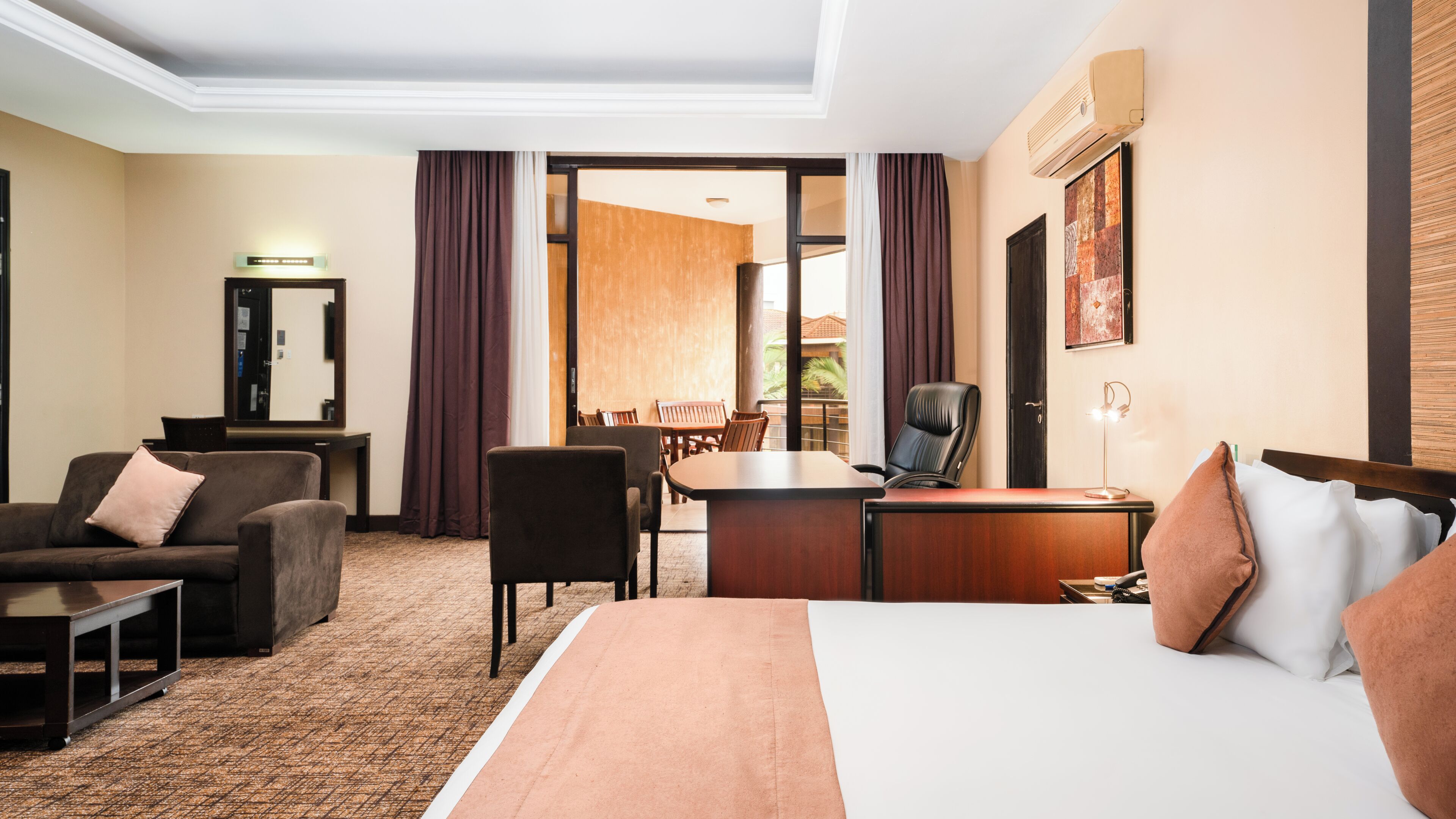 Habitación de hotel con cama, escritorio, silla, sofá, mesita y espejo.