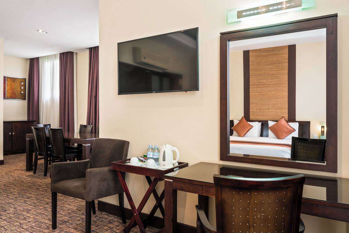 Habitación de hotel con televisión, cama con almohadas, escritorio con cafetera y una silla.
