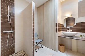 Une salle de bain avec une douche, un lavabo, un miroir et une petite chaise.