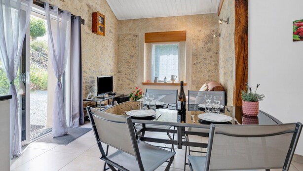 A dining area with a round table, chairs, a television, and a window with curtains. - Gîte Du Côteau – 10 min from Puy du Fou (Les Herbiers)