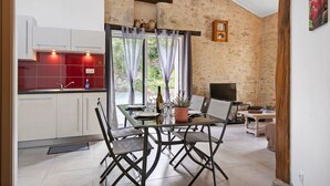 A modern kitchen with white cabinets, a red backsplash, and a dining area with a table and chairs. - Gîte Du Côteau – 10 min from Puy du Fou (Les Herbiers)