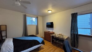 Een slaapkamer met een bed, bureau, stoel, televisie, plafondventilator en raam met gordijnen.