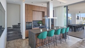 A modern kitchen with a central island, wooden cabinets, and a dining area with a large table and chairs. - Brand New 4 Bedroom Villa in Protaras Center (Paralimni)