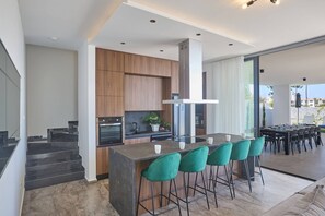 Eine moderne Küche mit einer zentralen Kochinsel, Holzschränken und einem Essbereich mit großem Tisch und Stühlen.